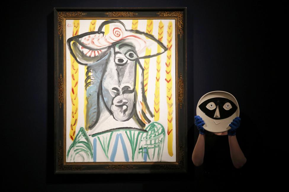 A member of staff poses with a ceramic plate by Picasso next to 'Tete' by Picasso at Christie's auction house in London